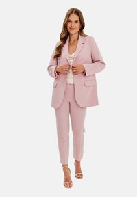 Jasnoróżowy klasyczny garnitur składający się z marynarki z klapami i dopasowanych spodni. Charakteryzuje się gładkim materiałem i minimalistycznym designem.
