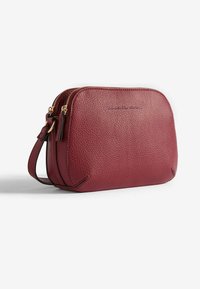 Piccola borsa a tracolla in pelle rossa con texture, dotata di due scomparti con zip e tracolla regolabile, esposta su sfondo bianco.