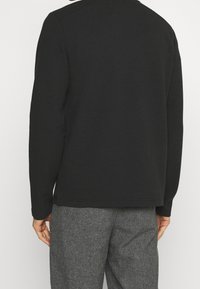 Schwarzer strukturierter Sweatshirt mit rundem Halsausschnitt, langen Ärmeln und lockerer Passform, kombiniert mit grauen gemusterten Hosen.