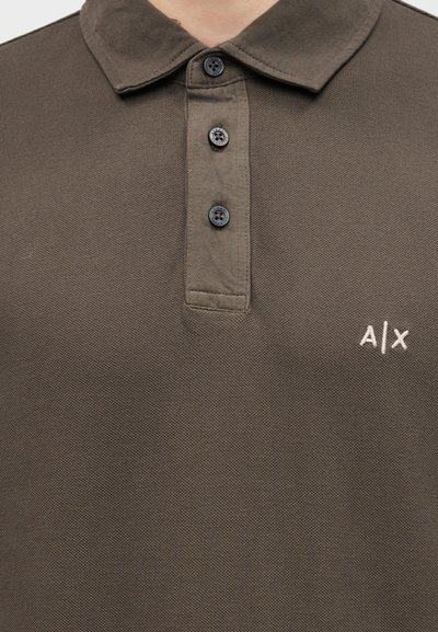 Polo marron texturé avec trois boutons noirs et logo "A|X" blanc brodé sur le côté gauche de la poitrine.