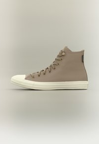 Beige high-top sneaker with textured upper, white rubber toe cap, and matching midsole. Features flat laces and metal eyelets.