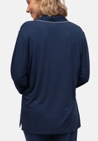 Top de manga larga azul marino hecho de una tela suave. Presenta un cuello con solapa y un ribete blanco a lo largo del cuello. Corte holgado con aberturas laterales.