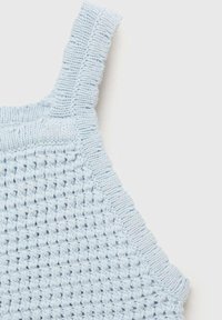 Svetlo modra pletenina z teksturirano mrežno vzorcem. Ima valovit rob ob trakovi za dodaten detajl.