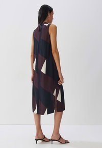 Ärmelloses Kleid in Dunkelblau und Burgunderrot mit weißen geometrischen Mustern. Verfügt über seitliche Schlitze und eine Knopfdetail am hinteren Halsauschnitt.