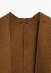Brun ullblazer med djup V-hals, inga knäppningar och en mjuk textur. Fodret har en etikett med "Massimo Dutti."