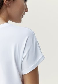 Witte kortebloes met een gladde textuur, voorzien van opgerolde mouwen en een klassieke ronde hals. Minimalistisch ontwerp, zonder patronen of accenten.