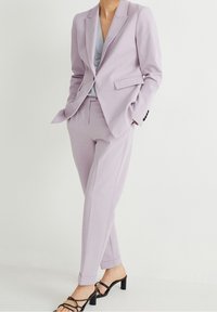 Jasnoliliowy dopasowany garnitur z marynarką zapinaną na guziki oraz spodniami o wąskim kroju. Połączony z szarym topem i czarnymi sandałami na cienkich paskach.