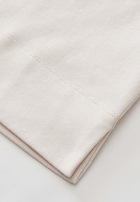 Hellbeige Baumwollstoff mit glatter Textur, der flache Nähte aufweist. Die Kanten sind ordentlich umgeschlagen und zeigen einen dezenten Glanz.