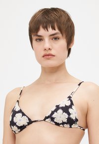 Fekete virágmintás bikini háromszög kialakítással, nagy krém színű virágokkal és vékony állítható pántokkal. Sima textúra és könnyű anyag.