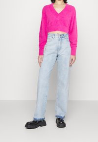 Flauschiger rosa kurz geschnittene Pullover mit V-Ausschnitt, kombiniert mit hellblauen geraden Jeans und schwarzen klobigen Plattformschuhen.