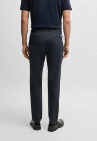 Dark navy trousers with a smooth texture, slim fit, and two rear zipped pockets. Paired with black shoes for a complete look.