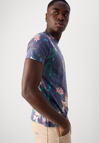 Camiseta de manga corta en azul marino con patrones florales coloridos, con un cuello redondo y una forma ajustada, hecha de tela suave y liviana.