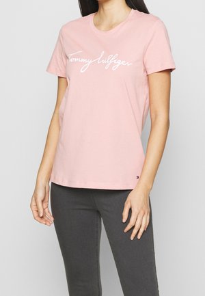 Roze katoenen T-shirt met korte mouwen en een ronde hals, met het witte "Tommy Hilfiger"-logo over de borst. Zachte textuur, ontspannen pasvorm.