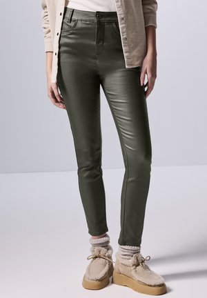 Pantaloni slim-fit di colore verde oliva, a vita alta, realizzati in un materiale liscio e lucido. Presentano tasche frontali e una chiusura con bottone. Abbinati a calzini comodi e scarpe.