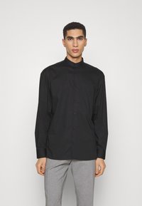 Camicia nera a maniche lunghe con colletto alto, chiusura frontale con bottoni e una tasca sul petto. Tessuto liscio con vestibilità su misura.