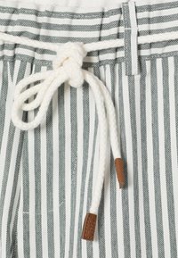 Λευκό και γκρι ύφασμα με κάθετες ρίγες και άσπρο πλεγμένο κορδόνι δεμένο σε φιόγκο μέσα από θηλιές ζώνης, με άκρα από δέρμα.