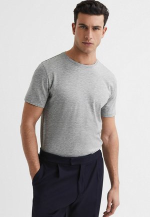 Camiseta gris de manga corta hecha de un tejido suave, con cuello redondo y un diseño ajustado, junto con pantalones oscuros. Sin patrones ni acentos visibles.