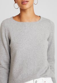 Szary sweter z dzianiny o okrągłym dekolcie i długich rękawach. Miękka tekstura, luźny krój, z widocznymi detalami przeszyć.