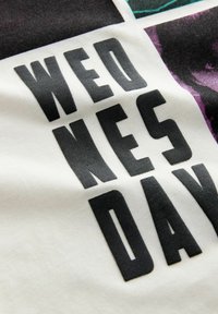 Tkanină albă cu un grafic imprimat negru care spune "WED NES DAY." Textul este prezentat într-un font îndrăzneț, de tip bloc, cu o ușoară strălucire.
