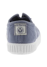 Blauwe canvas instap schoenen met een witte rubberen zool, met een rechthoekig label aan de achterkant met de merknaam "Victoria."