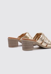 Sandalias de tacón metálico dorado con diseño plisado, tacones de bloque con textura de madera y parte superior de cuero suave. Estilo de punta abierta.