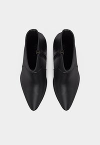 Μαύρα δερμάτινα μποτάκια αστραγάλου με μυτερά δάχτυλα και φερμουάρ στην εσωτερική πλευρά, εμφανιζόμενα από πάνω σε λευκό φόντο.