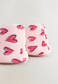 Pūkuotos rožinės pagalvėlės su raudonais širdies raštais, stačiakampio formos, minkšto tekstūros, suapvalintais kraštais ir subtiliu blizgesiu audinio paviršiuje.