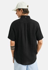Schwarzes Kurzarmhemd aus Leinen, mit klassischem Kragen, knöpfbarem Rücken, subtiler Textur und lockerer Passform.