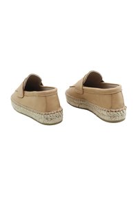 Zapatos de cuero marrón claro sin cordones con un tacón redondeado y suela de yute trenzado. Presentan una superficie lisa y un diseño minimalista sin herrajes visibles.