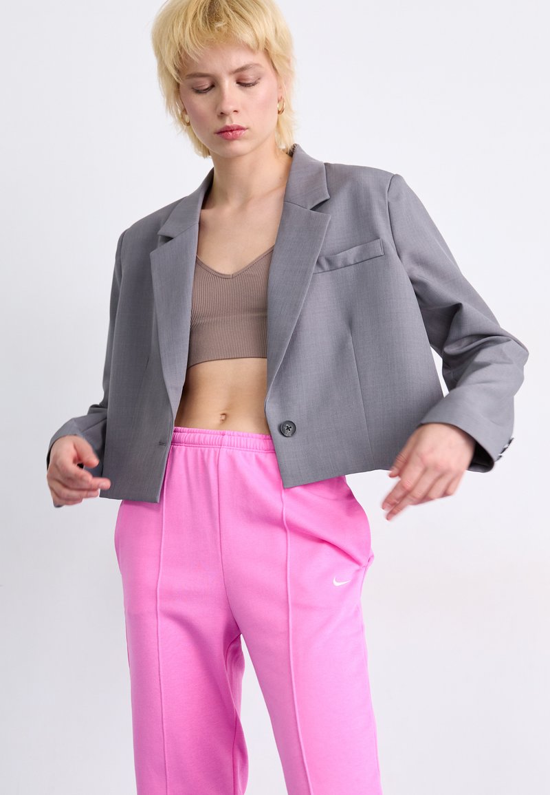 Grauer, taillierter Blazer mit einem Ein-Knopf-Verschluss und Tasche, kombiniert mit pinken Sweatpants mit seitlichem Streifen und Nike-Logo.