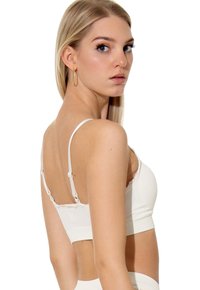 Bralette bianco a costine con spalline regolabili e bordi in pizzo. Presenta un design cropped e bordi senza cuciture per una vestibilità liscia.