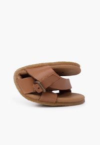 Sandale en cuir marron avec deux larges sangles, boucle réglable et doublure douce et texturée. Semelle plate aux bords arrondis, silhouette courbée.