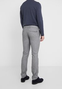 Harmaat ruudulliset housut slim fit -mallissa, joissa on takataskut ja vyölenkit, yhdistettynä tummansiniseen pitkähihaiseen paitoihin ja mustiin kenkiin.