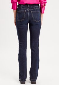 Dark blue denim flared jeans with a smooth texture, featuring two back pockets, and a subtle stitched detail along the seams.