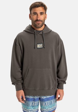 Mörkgrå hoodie med framficka och snoddar, med en liten logotypapplikation. Stylad med mönstrade blå och vita shorts.