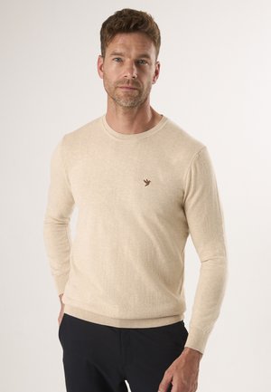 Beige gebreide trui met een ronde hals, lange mouwen en geribde manchetten. Bevat een klein bruin vogel logo op de linkerborst.