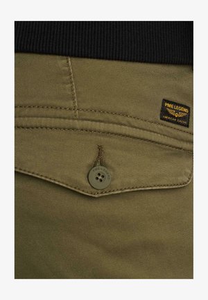 Gros plan sur la poche d'un pantalon vert olive avec fermeture par bouton et étiquette PME Legend au-dessus de la poche, sur un fond de ceinture noire.