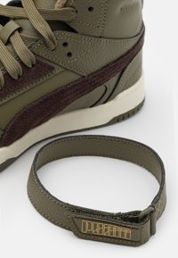 Grön läder hög sneaker med mörk lila mocka detaljer, texturerade material och beige sula. Inkluderar en matchande rem med en guld-logotyp.