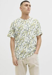 Tricou cu mânecă scurtă, confecționat dintr-un material ușor, având o bază bej cu un model de frunze verzi și albastre, decolteu rotund, croială lejeră.