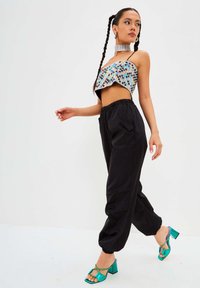 haut court à paillettes avec des motifs multicolores, pantalon cargo avec taille élastique noire, et sandales à talons blocs teal avec une sangle à la cheville.