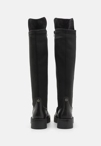 Bottes noires hauteur genoux avec un extérieur lisse et mat, doublure en tissu, fermeture éclair à l'arrière et détail de logo discret sur le talon.