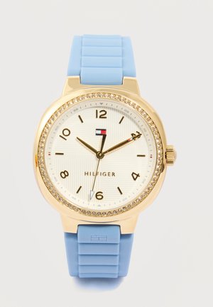 Gouden horloge met kristallen lunette, witte wijzerplaat, zwarte cijfers, blauwe siliconen band en drie wijzers die 10:10:30 aangeven.