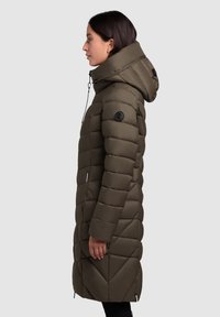 Garšs, olīvzaļš pūkains mētelis ar pūkām izšūtu dizainu, augstu apkakli, regulējamu kapuci un melnu logo uz pleca. Gluda tekstūra.