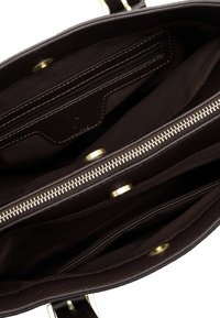 Interno di una borsa a tracolla in pelle marrone con una tasca con zip, due scomparti aperti e dettagli in metallo dorato. Texture liscia.
