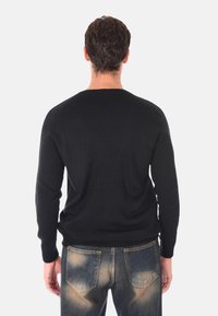Maglione nero a maglia con scollatura rotonda, maniche lunghe e polsini a coste, indossato con jeans blu sbiaditi, visto da dietro.