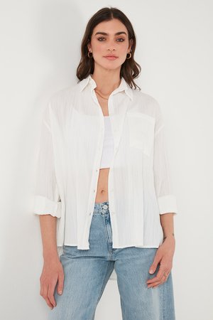 White, lightweight button-up shirt with a vertical striped texture, rolled sleeves, and a chest pocket, paired with high-waisted blue jeans.