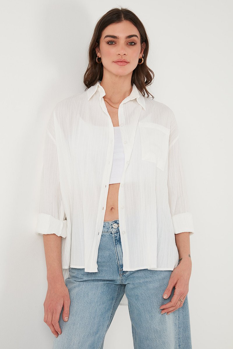 White, lightweight button-up shirt with a vertical striped texture, rolled sleeves, and a chest pocket, paired with high-waisted blue jeans.