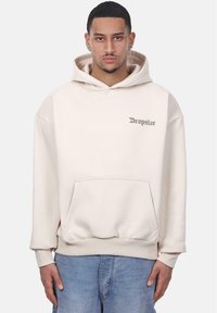 Beige Kapuzenpullover mit einer Fronttasche, Drop-Shoulder-Design und "Dropsize"-Text in Silber. Der Stoff wirkt weich und hat eine glatte Textur.