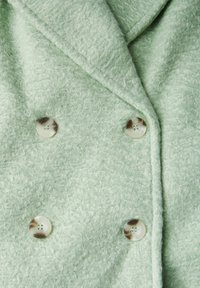 Cappotto in tessuto strutturato verde menta, con design doppiopetto e due bottoni rotondi a contrasto. Bordi lisci e cuciture a punto.
