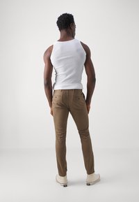 Débardeur blanc à côtes associé à un pantalon marron ajusté et des baskets blanches. Les pantalons sont dotés de poches arrière et d'une texture lisse.